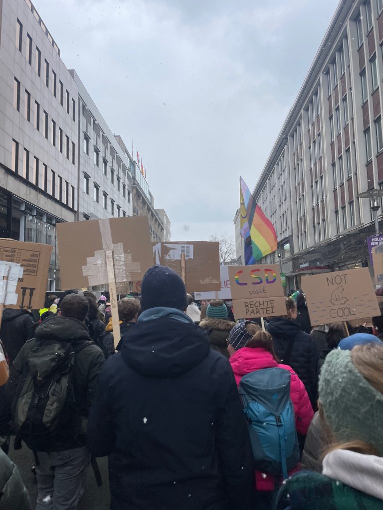 bei einer Demonstration halten Menschen Schilder mit Sprüchen darauf und Pride Fahnen hoch