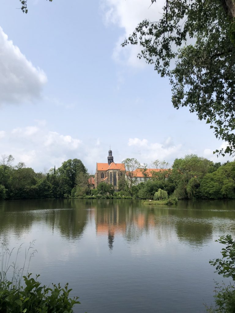 Foto von einem Teich im Vordergrund mit einem Kloster dahinter